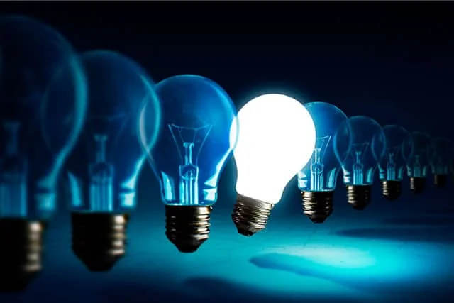 A lightbulb switches on amidst a row of other unlit bulbs to signify an innovative idea taking shape
