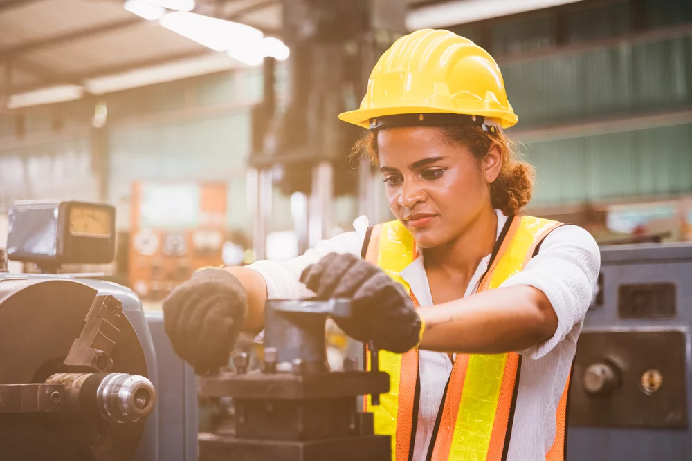 A woman wearing a high visibility jacket and hard hat operates machinery