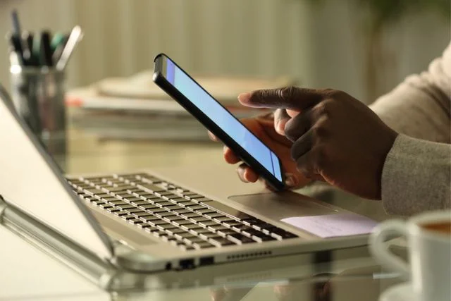 A pair of hands operating a phone and a laptop accessing the customer journey