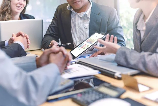 A meeting takes place at a table featuring tablets, laptops and smartphones