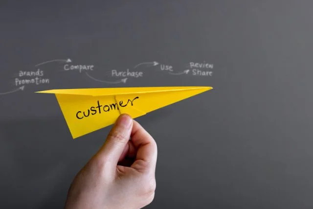 A paper aeroplane makes its way across a chalkboard displaying the customer journey