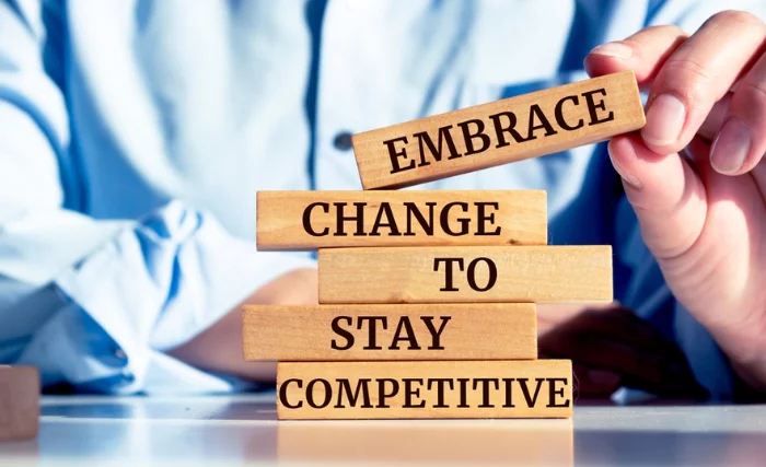 A hand stacks wooden blocks reading 'Embrace change to stay competitive.'