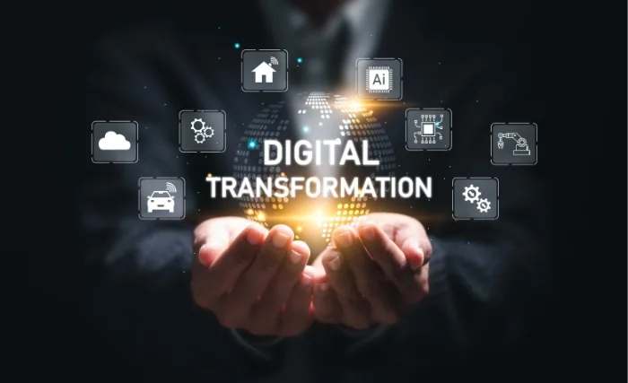 Businessperson holding a glowing “DIGITAL TRANSFORMATION” icon surrounded by floating tech and data symbols, representing innovation and connectivity.