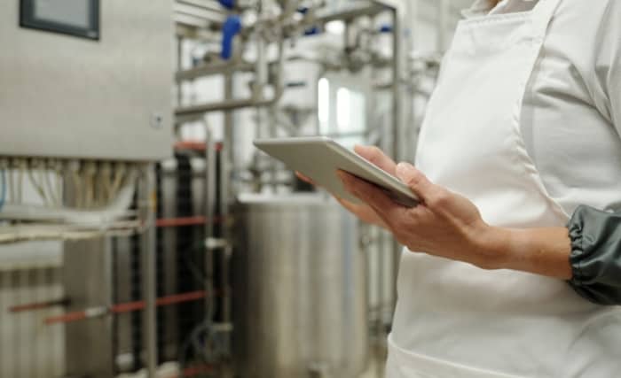 Close-up of food factory worker holding tablet near production equipment