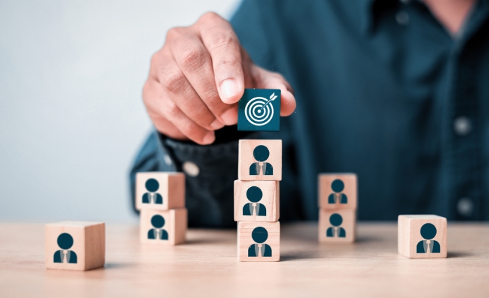 business resource planning: Hand placing target block on stacked employee icons, illustrating business resource planning, team structure, and goal-focused workforce management.