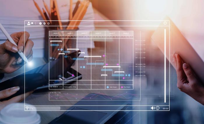How to get more from your existing marketing spend: A double-exposure image of two people working at a desk, overlaid with a transparent digital Gantt chart interface showing a multi-week project timeline with coloured task bars and line graphs.