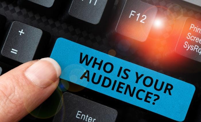 When less marketing focus works better: A close-up of a finger pressing a large blue keyboard key printed with the words "Who is your audience?" surrounded by dark keyboard keys, with an orange glow emanating from the F12 key above.