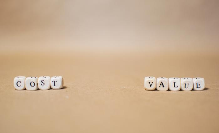 Why increasing marketing budget doesn't always improve results: Two groups of small white letter dice spelling "COST" and "VALUE" placed apart from each other on a plain beige surface.