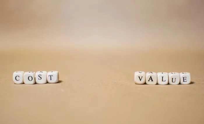 Why increasing marketing budget doesn't always improve results: Two groups of small white letter dice spelling "COST" and "VALUE" placed apart from each other on a plain beige surface.