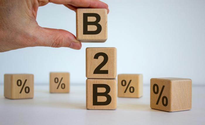 Understanding How B2B Buyers Actually Make Decisions
A hand places the letter "B" on top of two stacked wooden blocks spelling "B2B", with four additional blocks bearing percentage symbols arranged in the background.