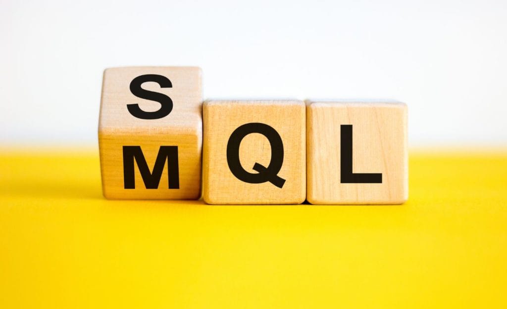 fixing the gap between sales and marketing: Wooden blocks on a yellow surface, with the first block turning from M to S to change MQL into SQL.