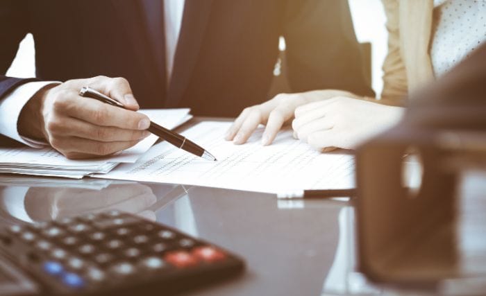 how does inheritance tax affect business succession: A man in a suit points a pen at a financial document while a woman beside him rests her hands on the paperwork. They’re at a glass desk with a calculator in the foreground.